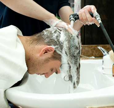 Side view of young man bending forward having hair washed in barbershop