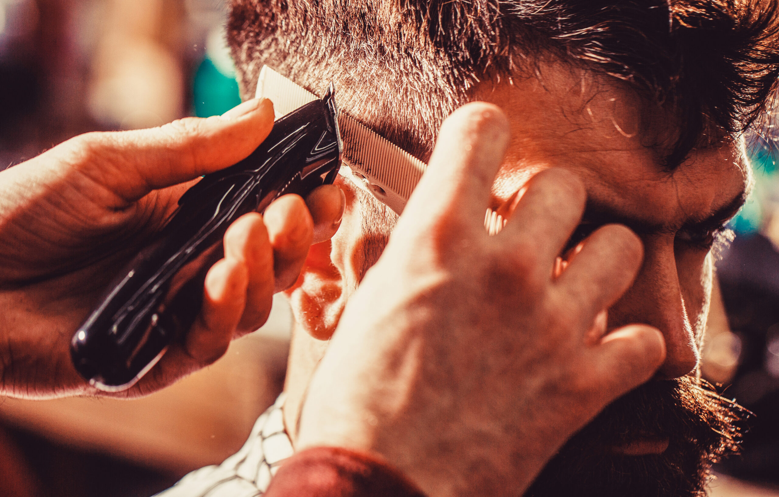 Barber works with hair clipper. Hipster client getting haircut. Hands of barber with hair clipper, close up